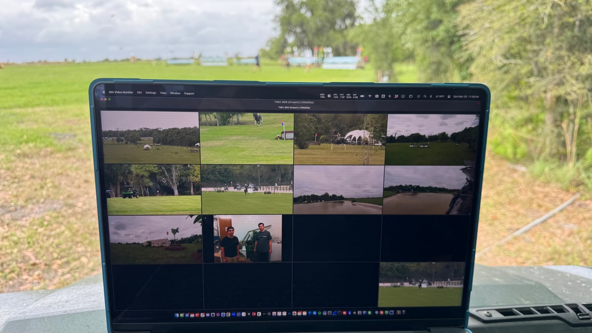 A laptop running an NDI multiview of every camera feed, set up on a stand out in the open field with the course behind it.