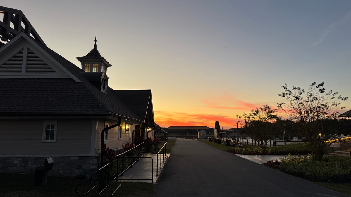 A barn pavilion with a cupola silhouetted against an orange sunrise sky, a paved path leading past it.
