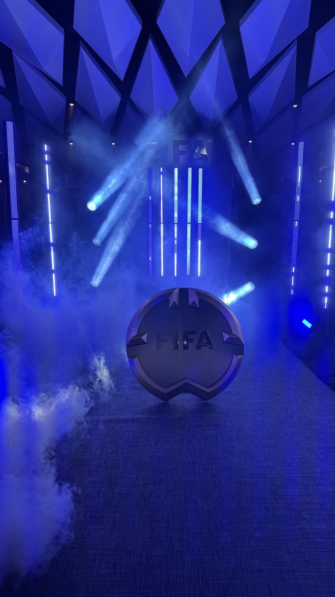 A FIFA crest sculpture in a haze-filled entrance, lit in deep blue with narrow beams overhead.