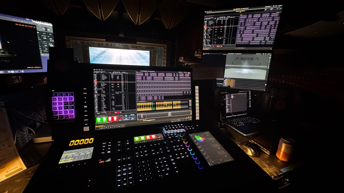 Same programming desk angle as the prior shot, different cue moment, different stage projection visible