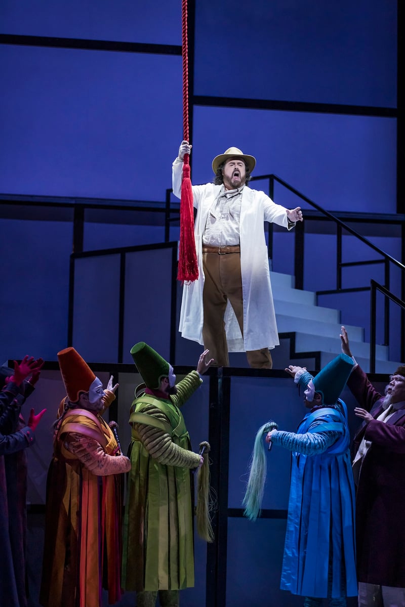 Jonathan Burton as Prince Calaf in a white coat ringing the gong, the three masked ministers reaching up below him, in The Atlanta Opera Turandot