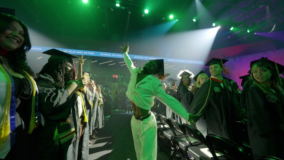 A dancer in a mint-green outfit strikes a pose in the aisle amid a green wash as graduates film and cheer on either side.