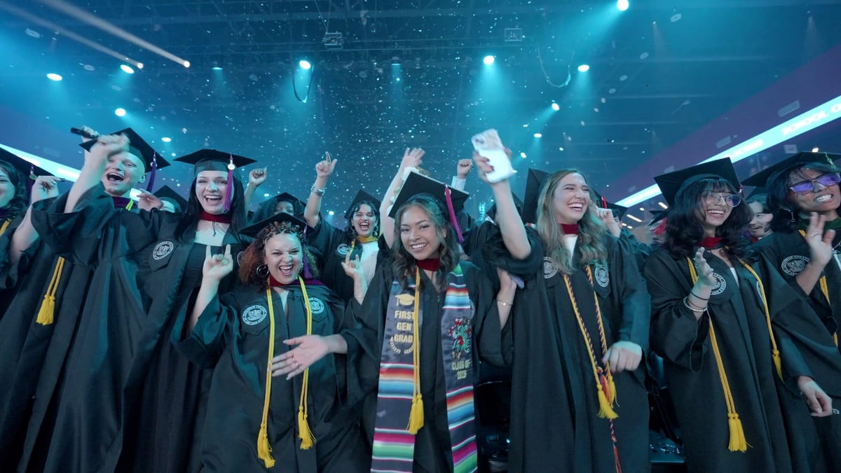 Beaming graduates celebrate with raised fists and phones under a teal wash and falling confetti, a first-generation-graduate stole in the center.