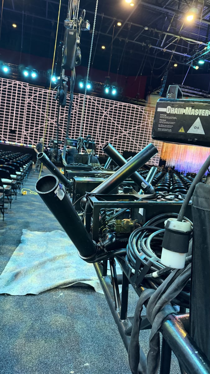 A lighting truss laid out on the deck during load-in, a ChainMaster hoist and coiled feeder cable alongside it, moving lights and the LED wall waiting in the background.