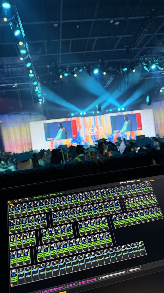 Running the ceremony from the console: an ETC Eos magic sheet on screen while blue beams sweep the stage, the 'SCAD' LED screens and a sea of caps and gowns beyond.