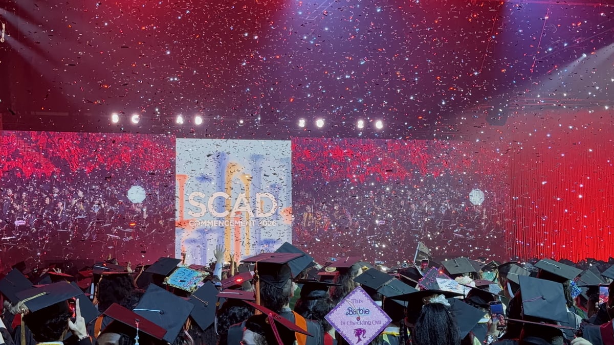 The confetti finale from within the graduating class, mortarboards filling the frame under a red wash and the 'SCAD Commencement 2026' screen.