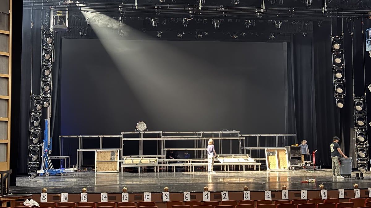 A big top-light beam over the tiered set during a cue.