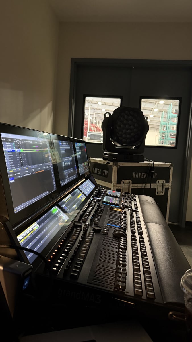 A grandMA console at the tech table, a moving light on a road case behind.
