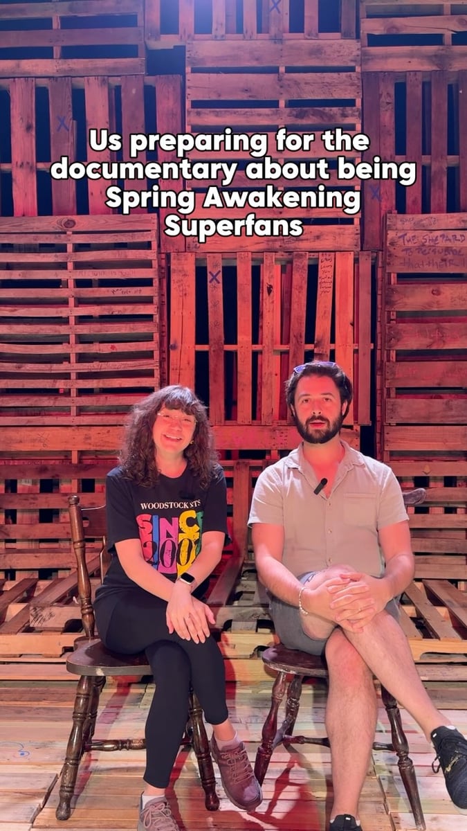 Two Woodstock Arts company members sit on wooden chairs before the red-lit pallet wall in a promo reel captioned about being Spring Awakening superfans.