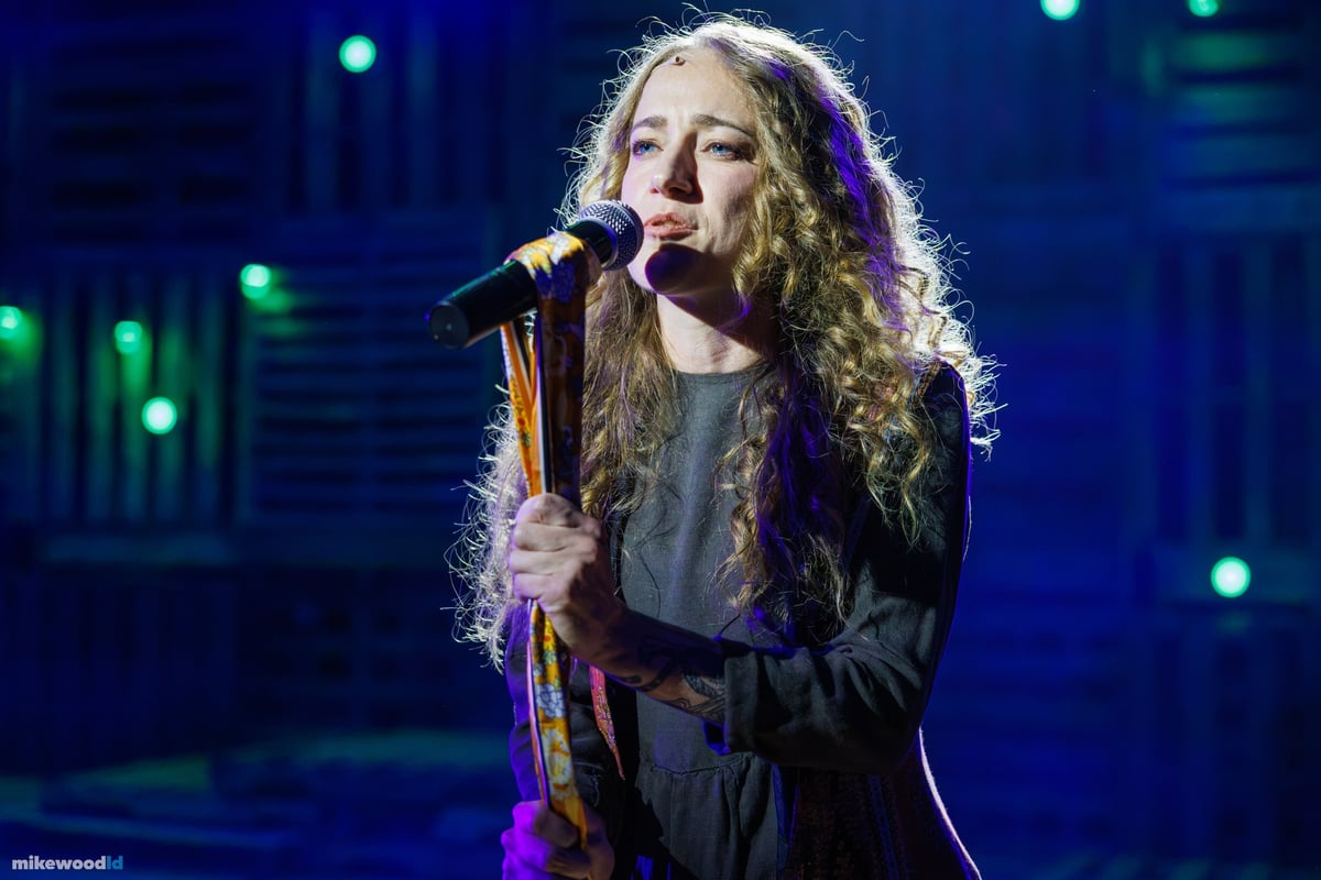A tight close-up of a young woman singing into a microphone, lit in deep blue.