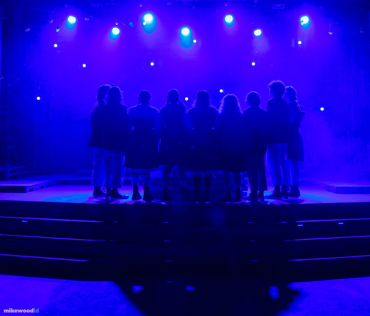 The young women stand clustered with their backs to us, silhouetted against an intense blue backlight thick with haze.