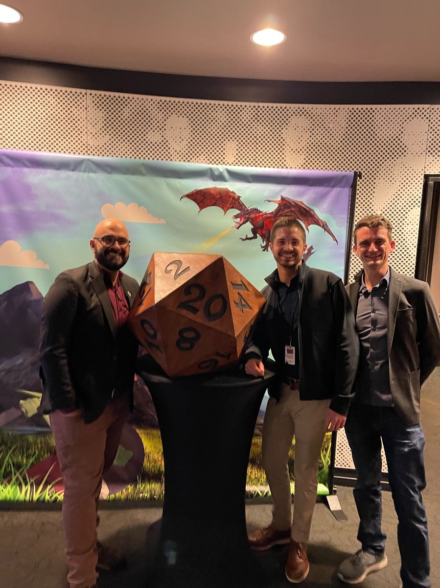 The creative team with the show's giant twenty-sided die prop in front of the fantasy backdrop.