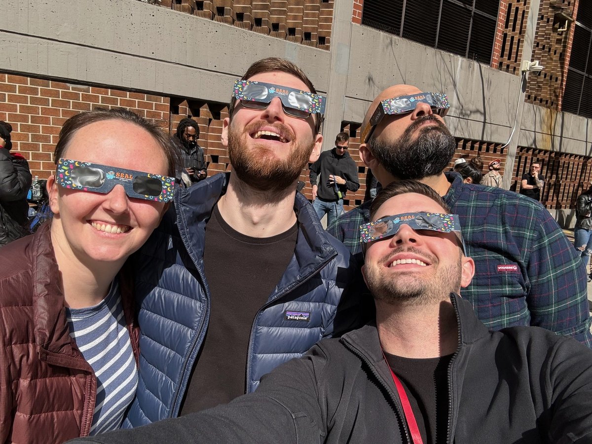 Four of the team outdoors in solar eclipse glasses, looking up at the sky during the April 2024 eclipse.