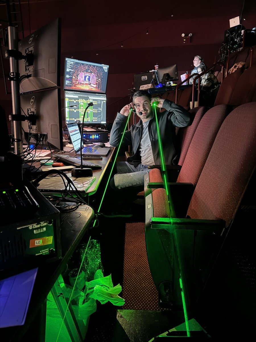 A designer at the house tech table mugging for the camera as green laser beams cut across the seats during a tech check.