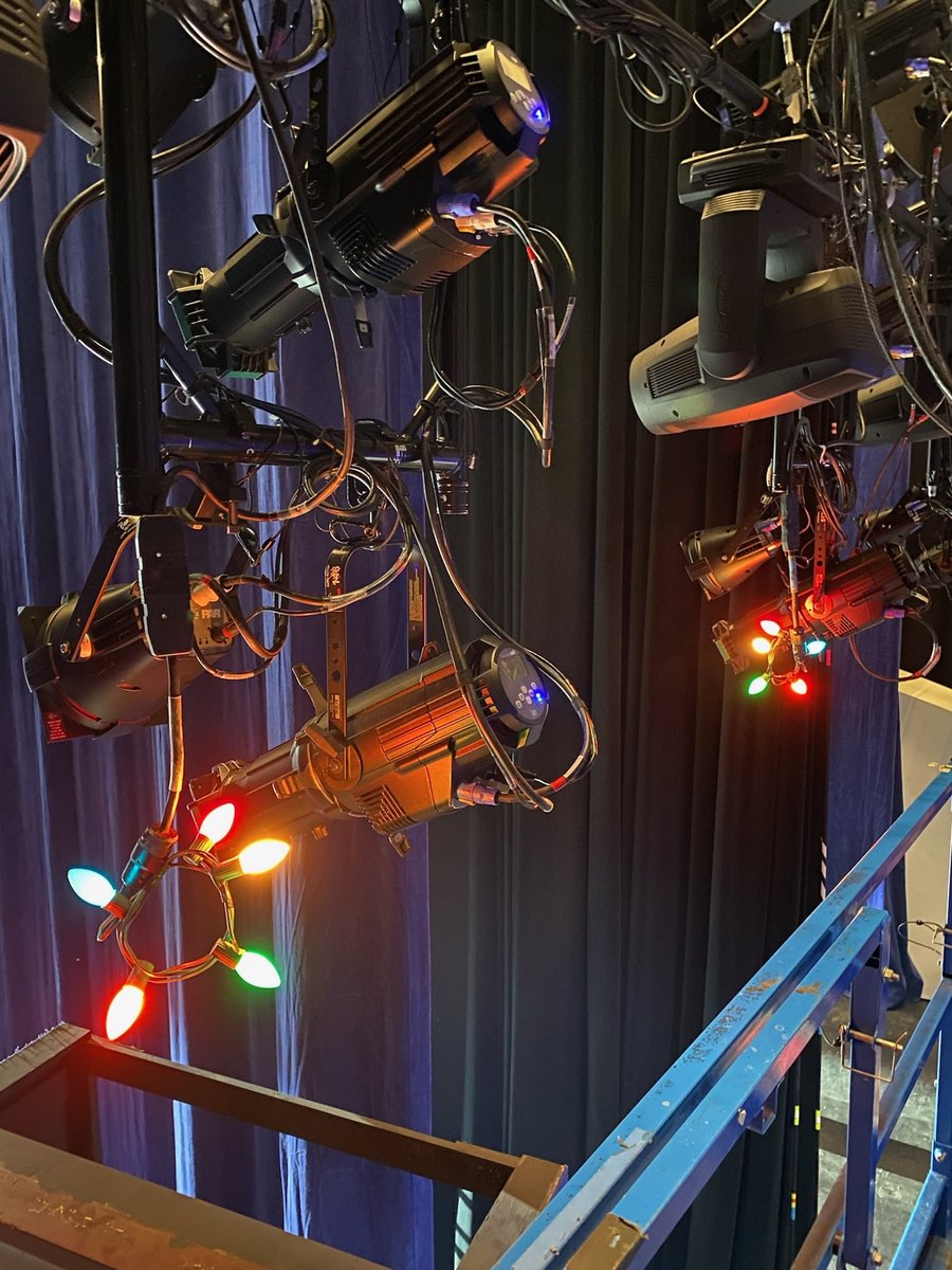 Lighting fixtures rigged on an electric strung with red and green holiday lights.