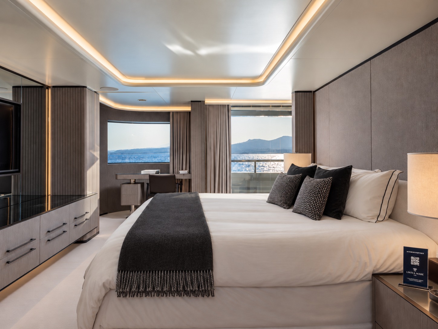 The full-beam master suite aboard M/Y Inari, dressed with Lintea Mare cushions and a fringed throw, with panoramic windows over the sea