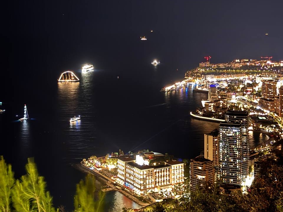 Monaco di notte durante il Monaco Yacht Show, con i superyacht illuminati alla fonda nella baia di fronte a Monte-Carlo