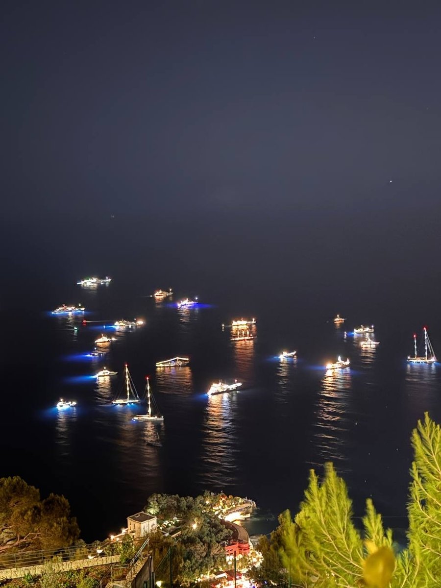 Superyacht e barche a vela alla fonda davanti a Monaco di notte, illuminati dalle luci subacquee
