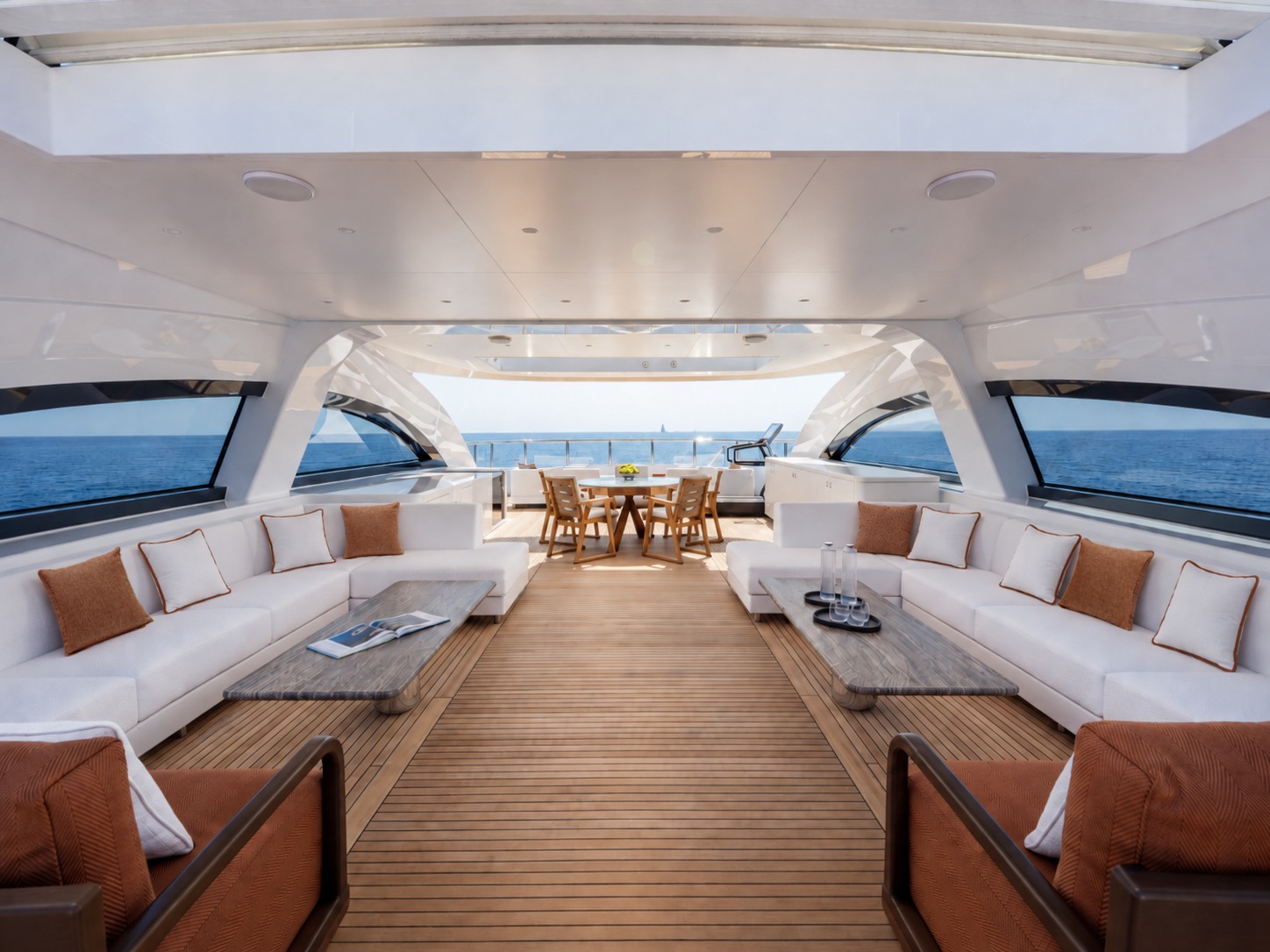 The flybridge lounge aboard M/Y Inari, with Lintea Mare cushions in terracotta and cream on facing sofas and a dining table beyond