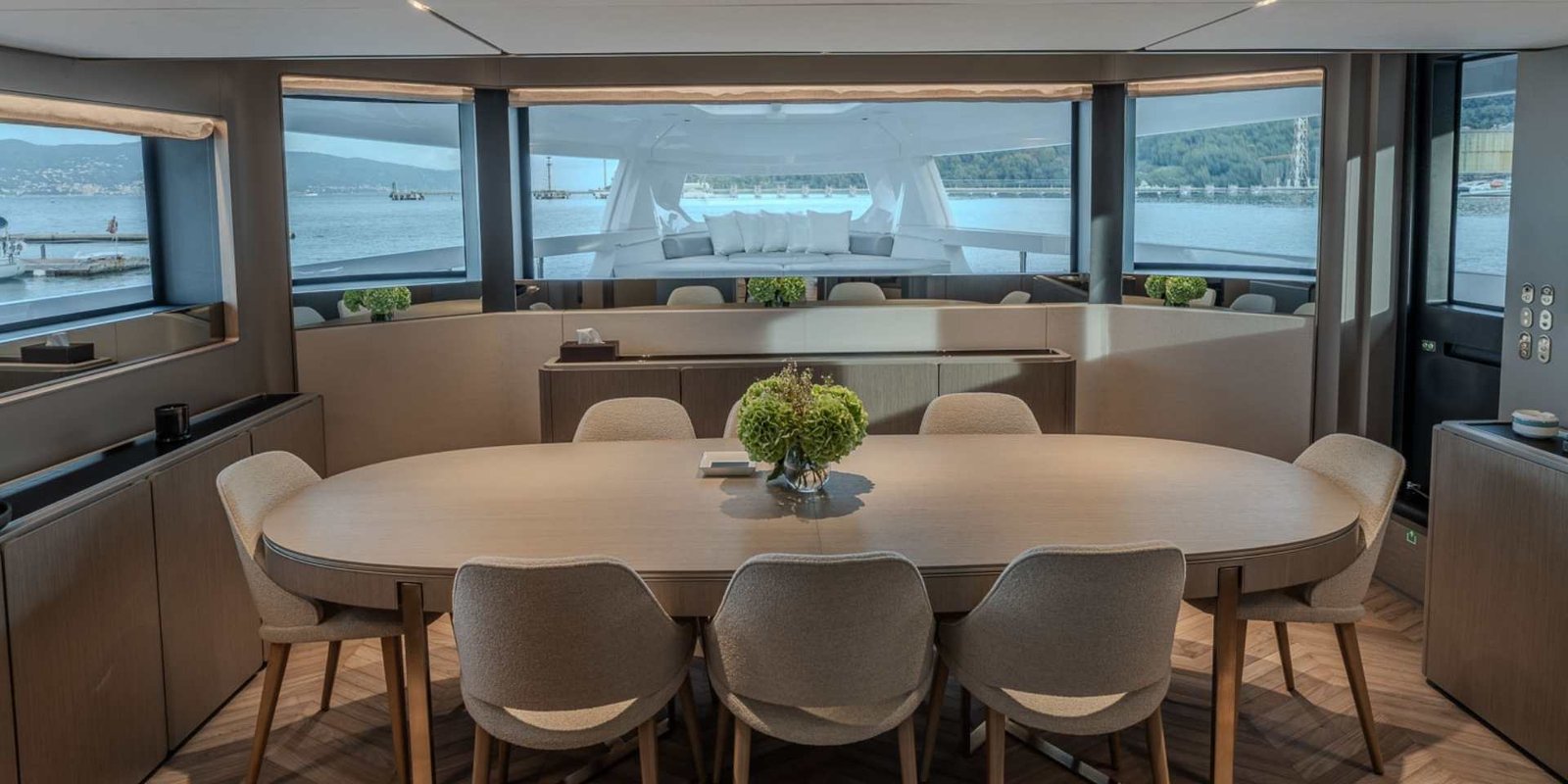 Tavolo da pranzo ovale sul ponte principale del Ferretti Infynito 90, con ampie finestrature su tre lati e la zona lounge di prua visibile oltre le vetrate frontali