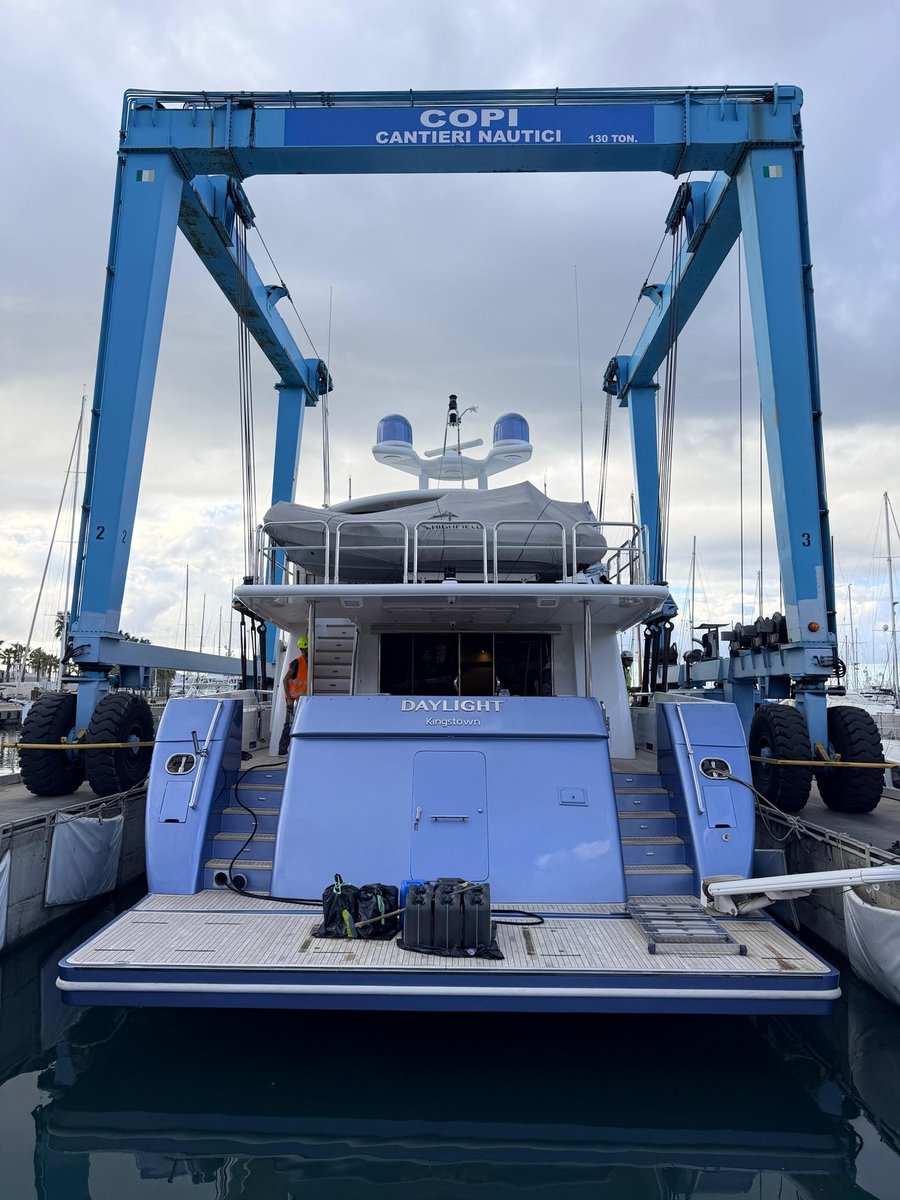 M/Y Daylight afloat in the travel-lift bay at Copi Cantieri Nautici, stern-on beneath the blue 130-ton lift, with her name and port of registry on the transom