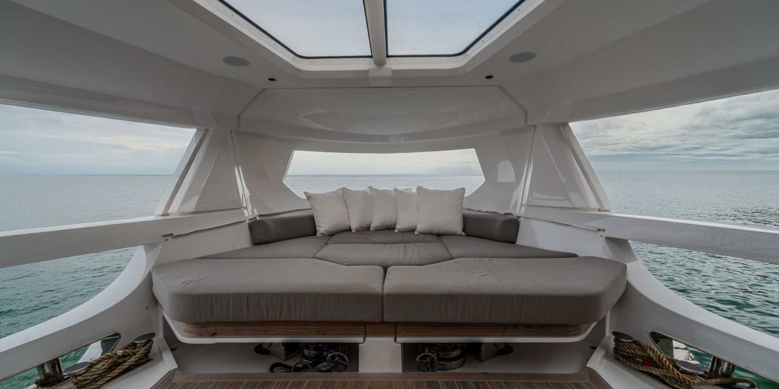 Zona lounge riparata a prua del Ferretti Infynito 90, con un ampio divano sotto il lucernario dell'hardtop e vista sul mare da entrambi i lati