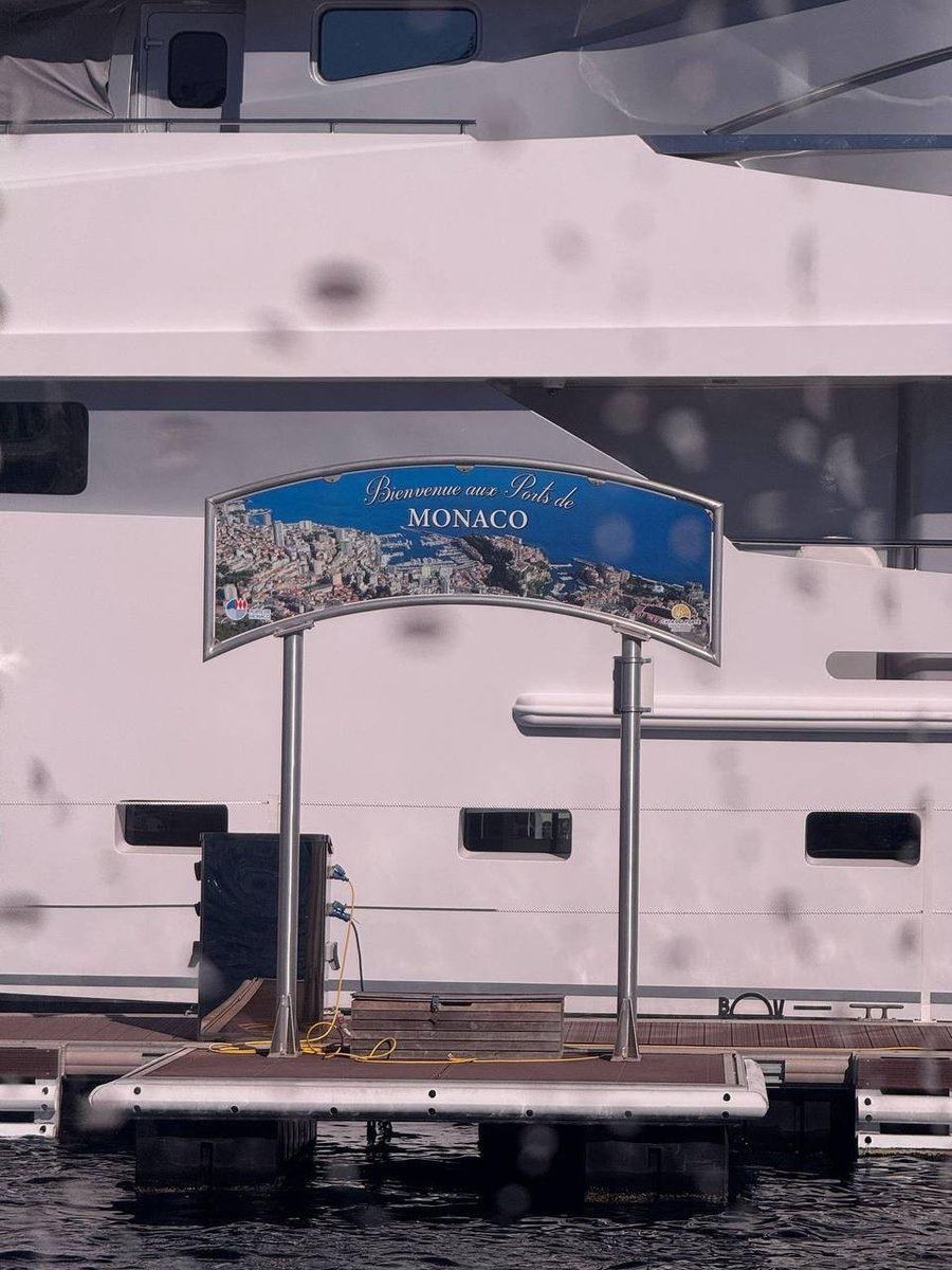 Cartello di benvenuto Ports de Monaco su un pontile di Port Hercule, davanti alla carena di un superyacht