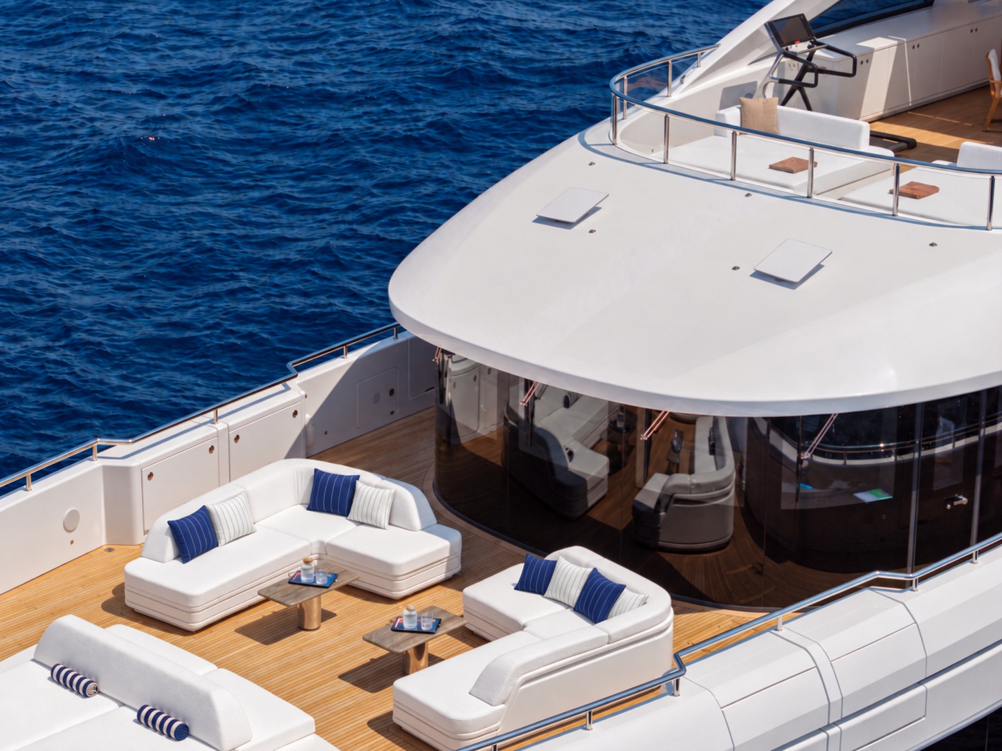 The aft deck lounge of M/Y Inari seen from the deck above, with navy and white Lintea Mare cushions on white sofas over teak
