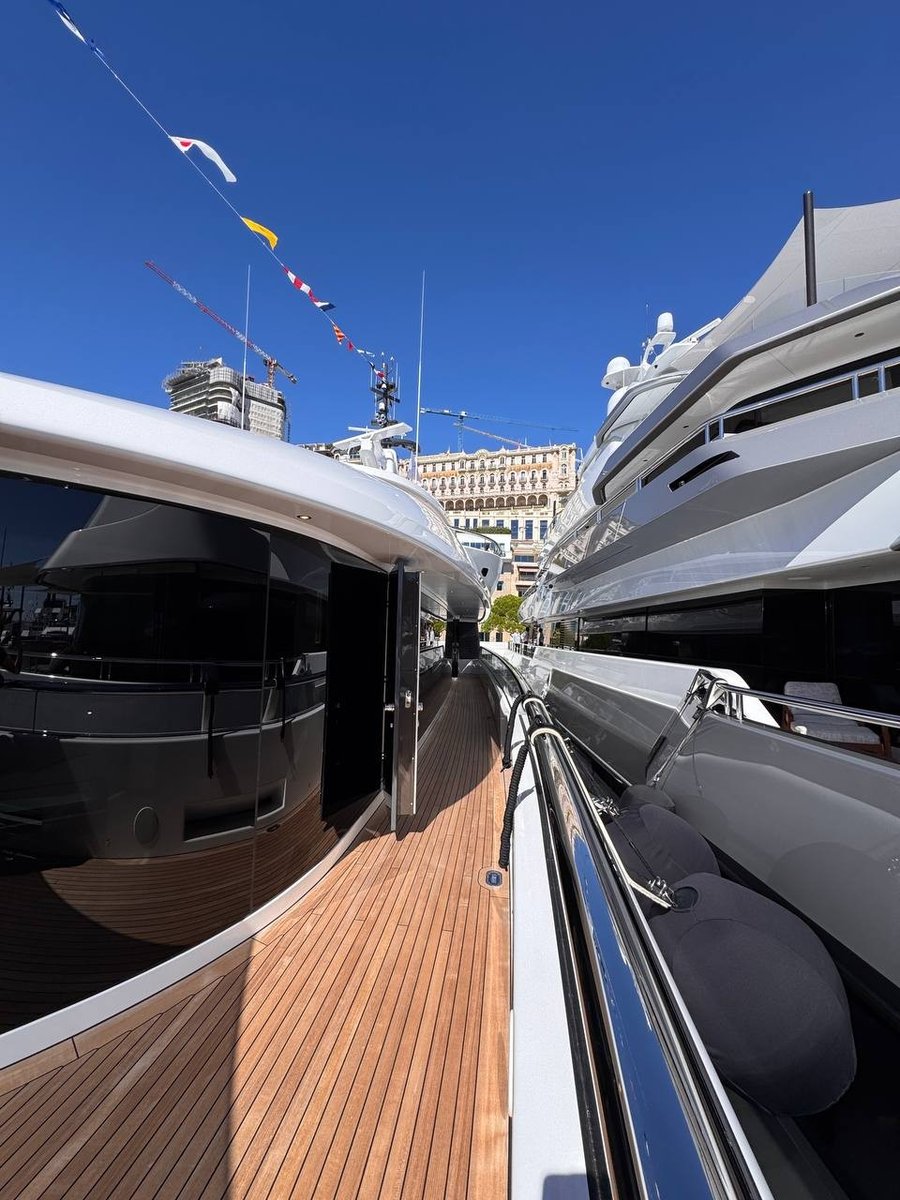Ponte laterale in teak di un superyacht ormeggiato di poppa a Port Hercule, con le bandiere di segnalazione e il profilo di Monte-Carlo sullo sfondo