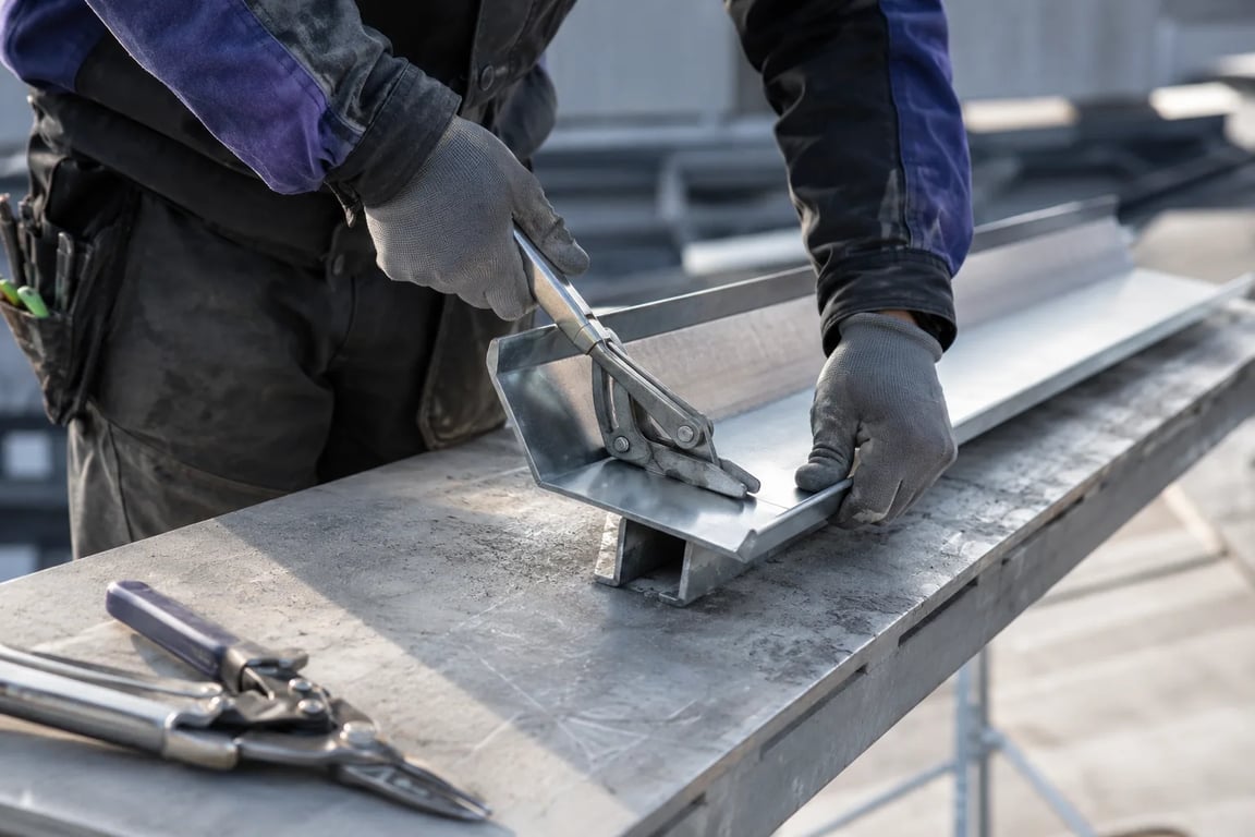 Nærbilde av blikkenslagerens hender som bukker sinkplate på en kantebenk