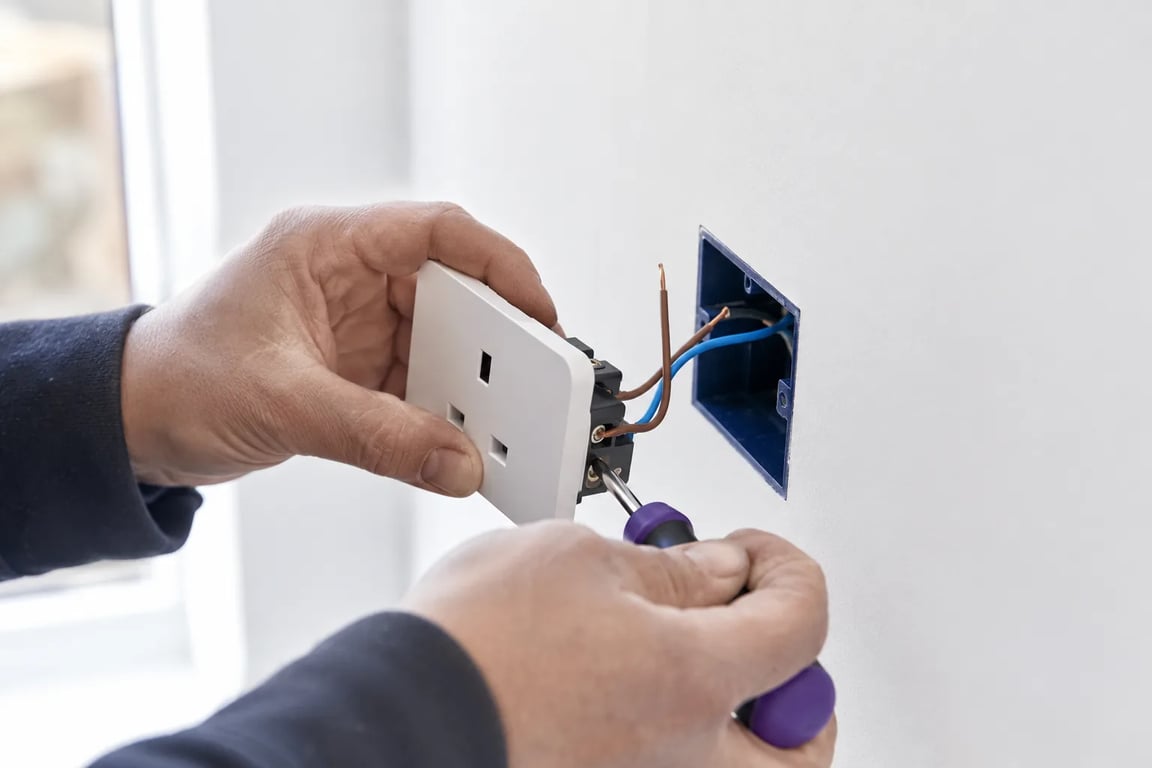 Nærbilde av elektrikerens hender som kobler en stikkontakt i veggboks
