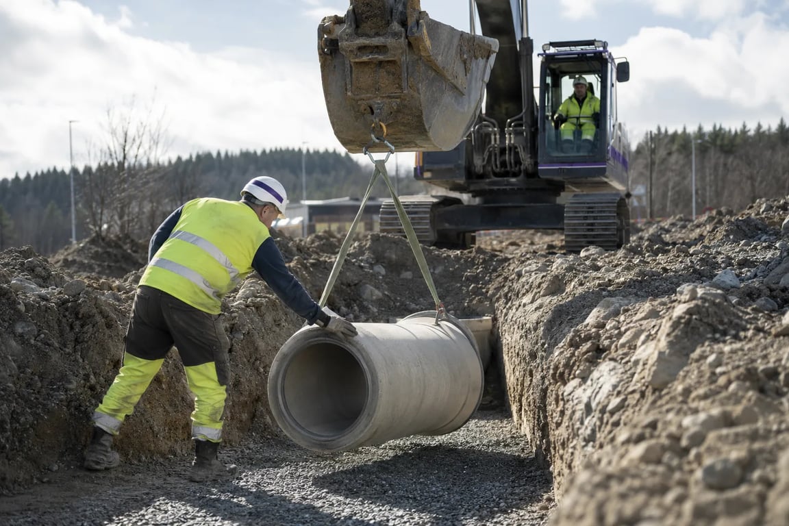 Anleggsarbeider styrer nedlegging av et betongrør i en grøft med gravemaskin