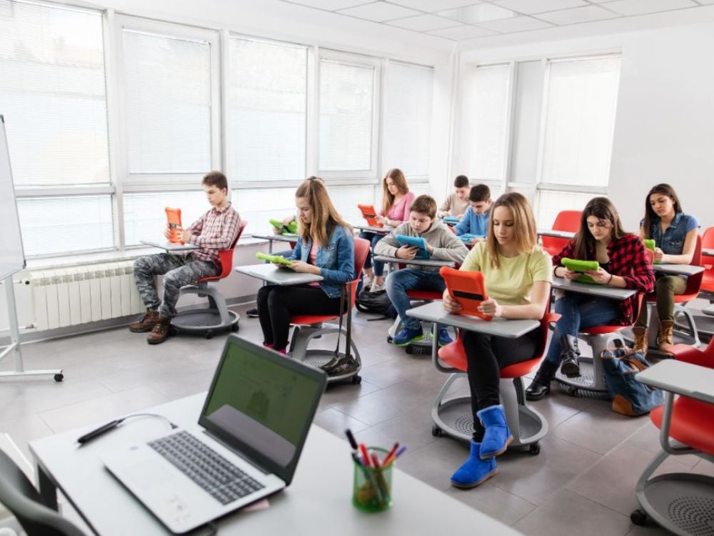 Sala moderna de aula com estudantes usando tablets, em ambiente de aprendizagem digital