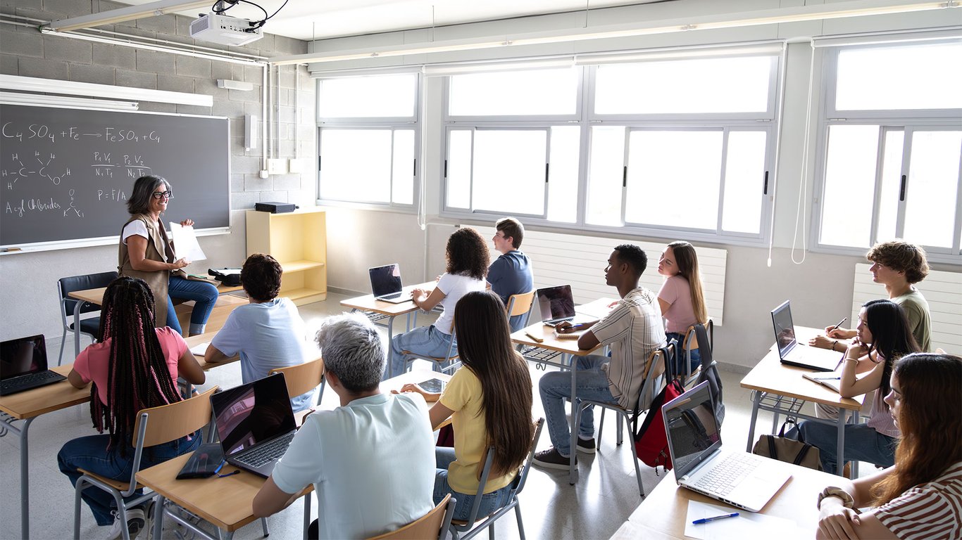 Sala de aula de tecnologia com professora e estudantes utilizando laptops