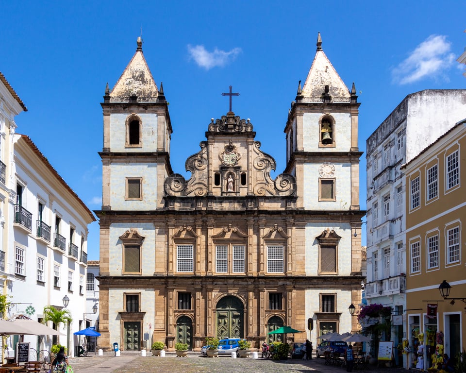 Paisagem urbana de cidade pequena na Bahia, com igreja histórica e praça central; montanhas ao fundo e céu aberto