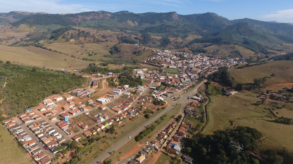 Vista aérea de cidade do interior às margens de um rio, com morros ao fundo, em fim de tarde