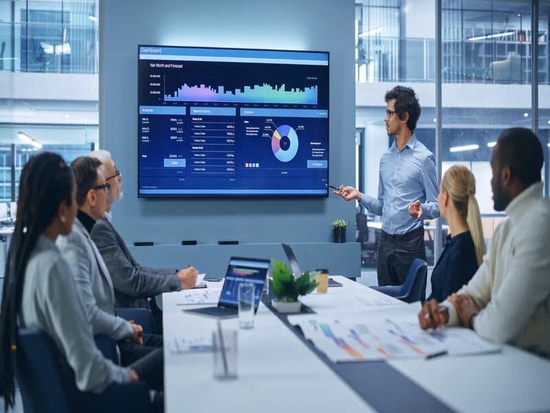 Ambiente corporativo de tecnologia com equipe reunida diante de apresentação em tela; contexto alusivo à área de TI