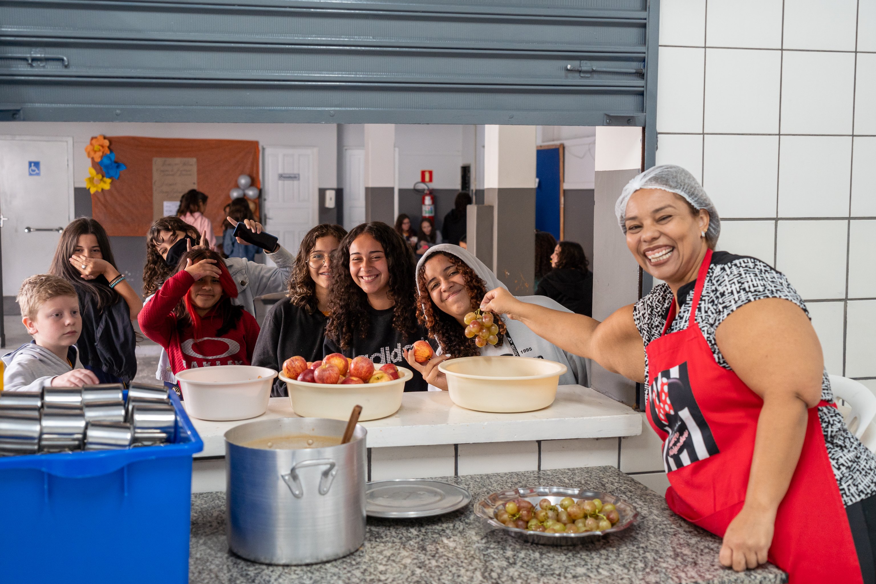Cozinha comunitária servindo frutas para crianças, com bancadas de inox e utensílios