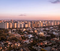 Foto aérea do skyline de Curitiba, com edifícios modernos e áreas verdes ao pôr do sol.