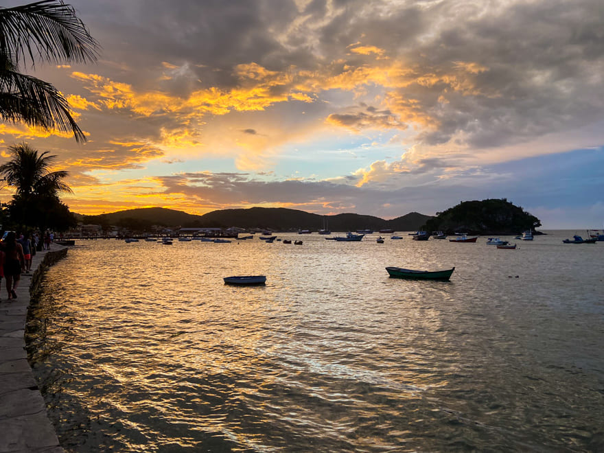 Vista costeira de Armação dos Búzios ao pôr do sol, com barcos e casas ao fundo