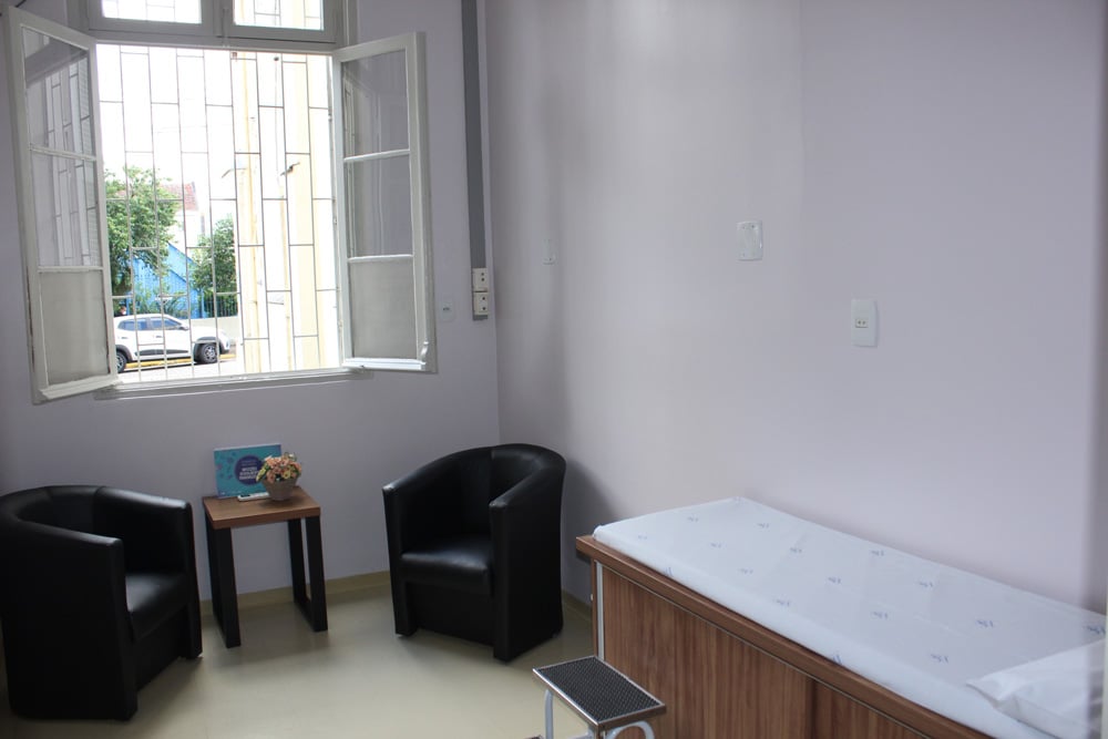 Ambiente clínico iluminado com mesa, cadeiras e materiais terapêuticos.