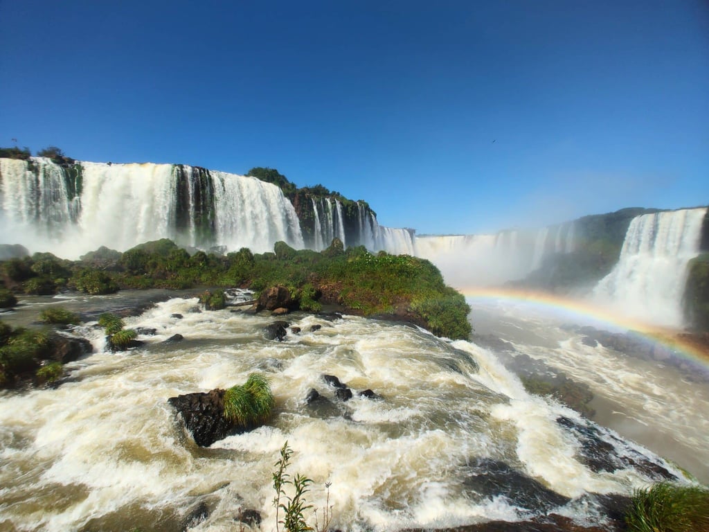 Cataratas do Iguaçu em dia ensolarado, com arco-íris e passarela de observação