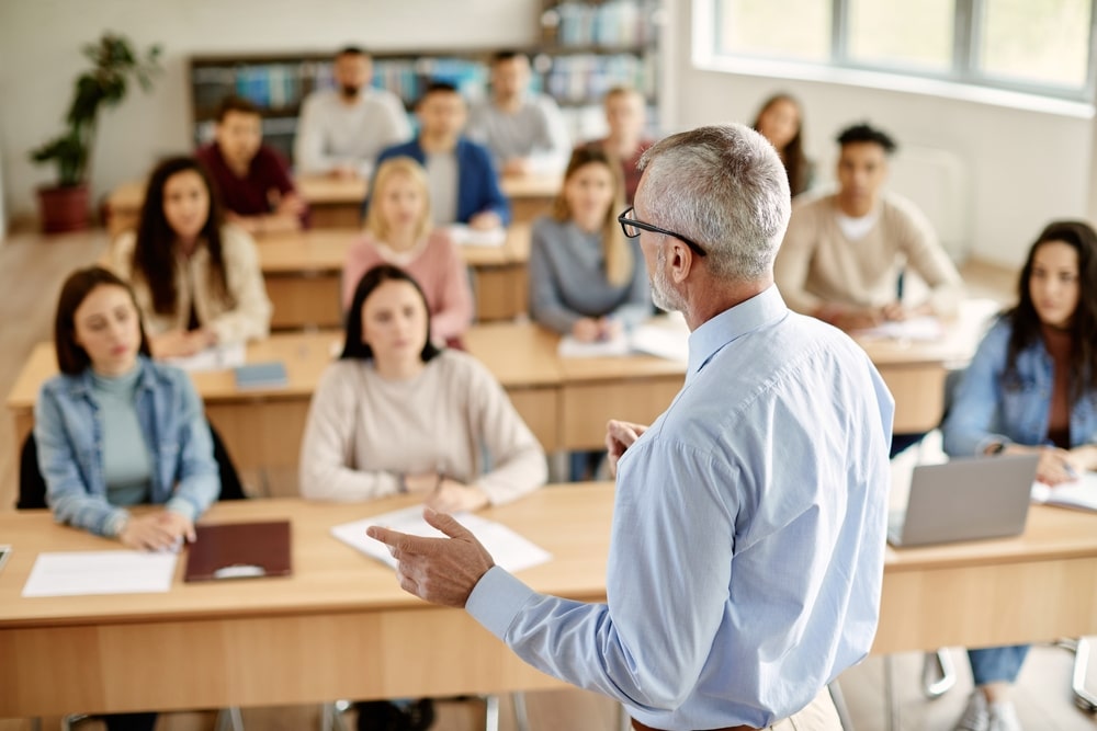 Professor conduzindo aula em instituição de ensino superior, com estudantes em sala