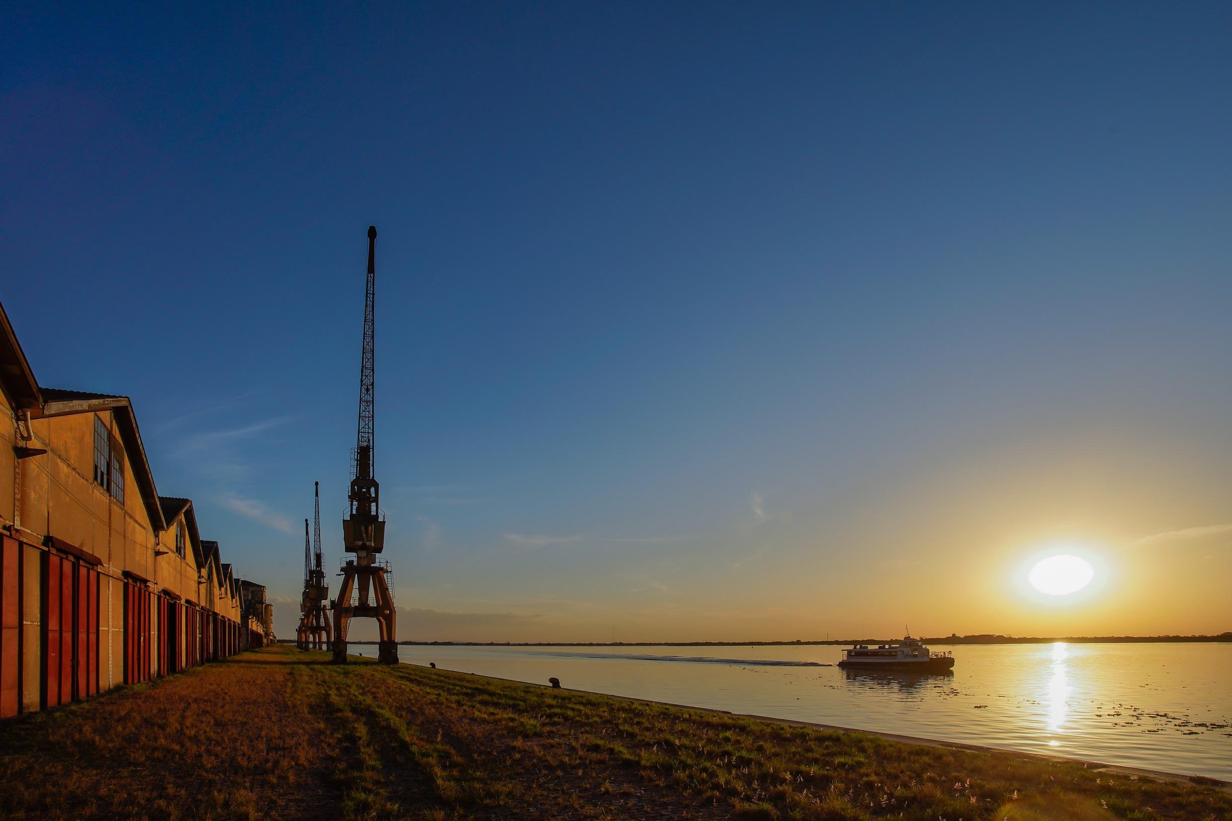 Pôr do sol no Lago Guaíba, com skyline de Porto Alegre e o Cais Embarcadero ao fundo; imagem horizontal ampla