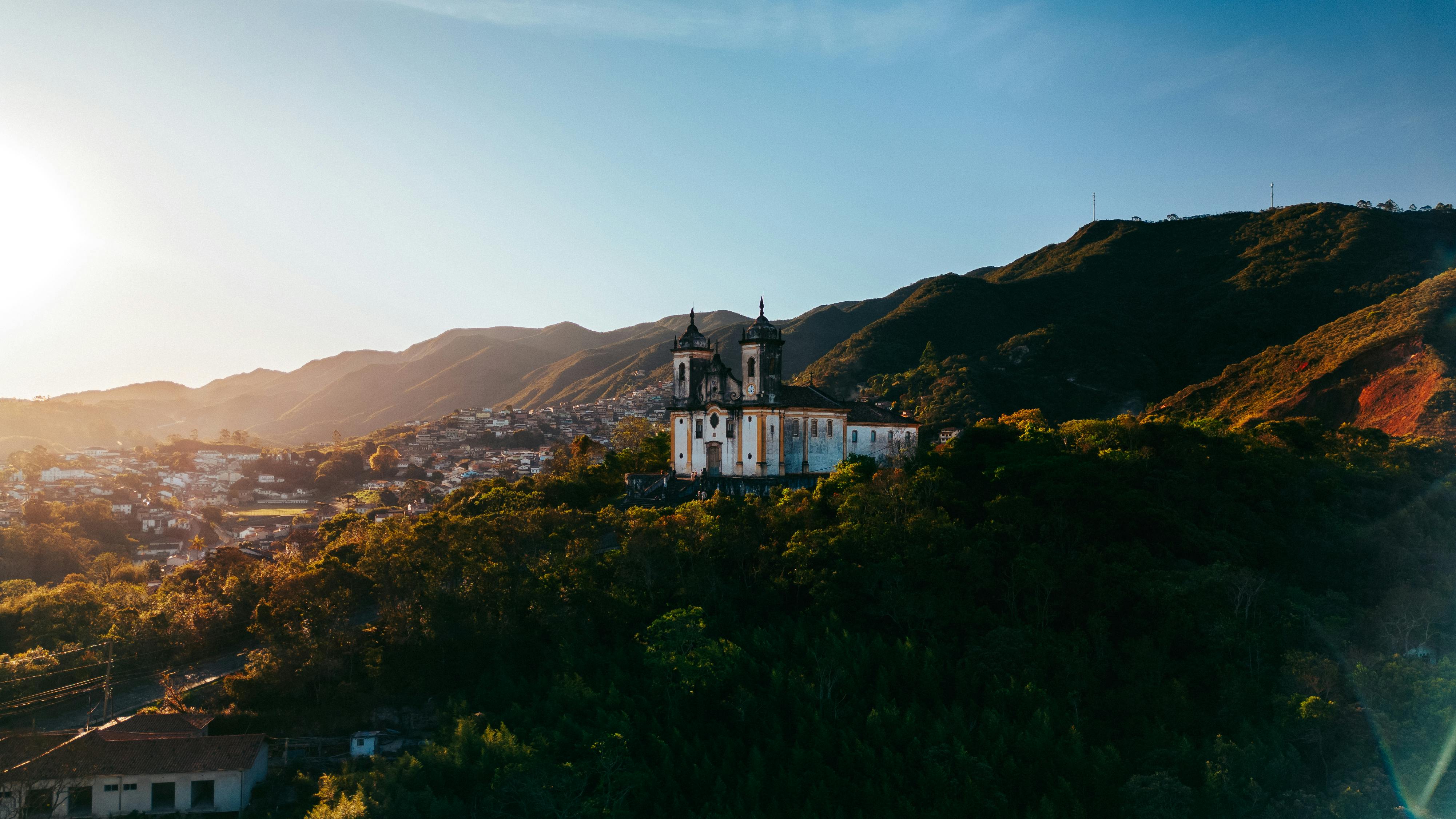 Vista aérea de cidade mineira com igreja e morros ao fundo ao pôr do sol