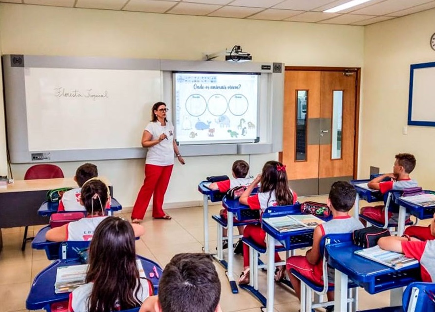 Sala de aula de tecnologia com quadro digital e alunos; foco em ensino de informática