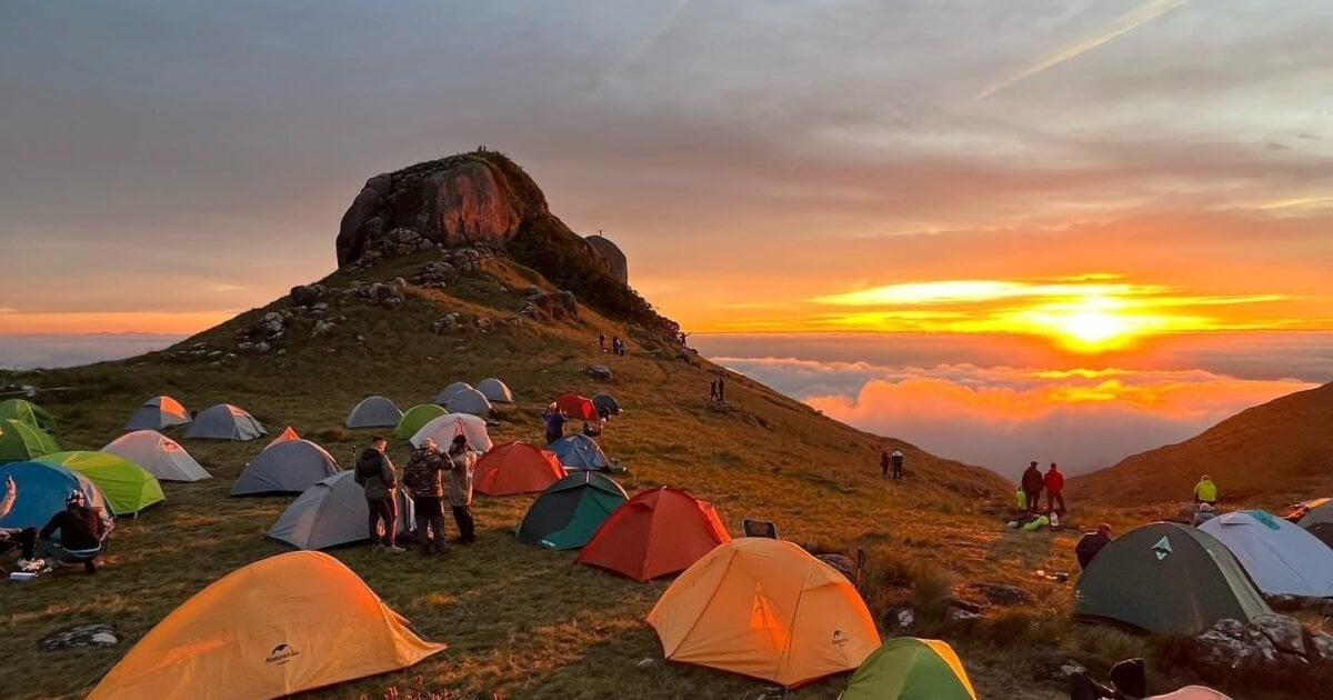 Paisagem de natureza serrana ao pôr do sol, com acampamento ao ar livre e montanhas ao fundo, remetendo a regiões de turismo de natureza como a Serra do Quiriri, em SC