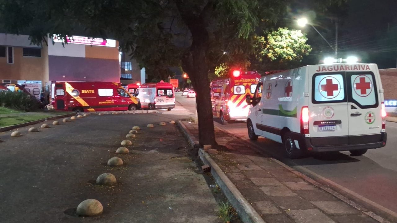 Fachada externa de hospital público com ambulâncias estacionadas, noturna
