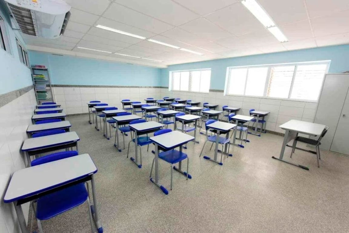 Sala de aula pública organizada e iluminada, carteiras enfileiradas e quadro