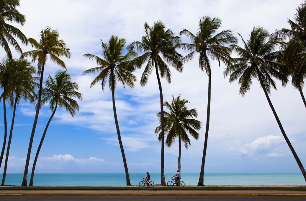 Orla de Maceió com mar azul-turquesa, ciclistas e coqueiros